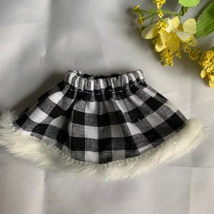 May include: A miniature skirt with a black and white checkered pattern. The skirt has a white fluffy trim along the bottom edge. The skirt is likely for a doll or other small figure.