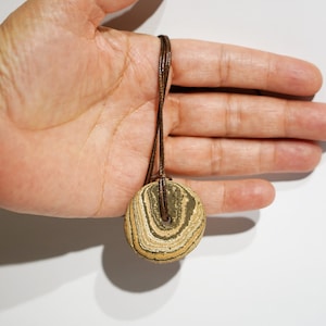 May include: A brown leather cord necklace with a round, layered, brown and white stone pendant.