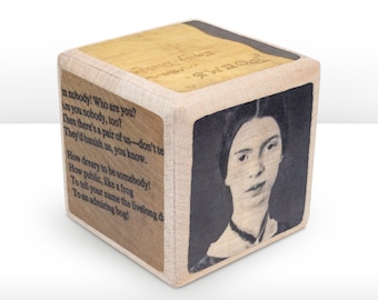 Könnte beinhalten: Ein Holzwürfel mit einem Schwarzweißporträt von Emily Dickinson auf der einen Seite und einem Gedicht von ihr auf der anderen. Das Gedicht lautet "im nobody! Who are you? Are you nobody, too? Then there's a pair of us-don't tell! They'd banish us, you know. How dreary to be somebody! How public, like a frog To tell your name the livelong day To an admiring bog!"