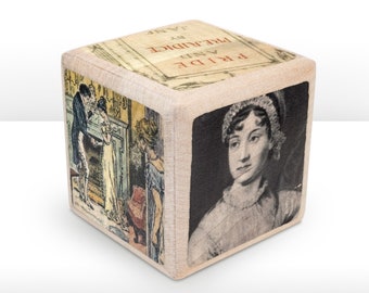 May include: A wooden cube with a beige fabric cover. The cube has four sides with images from the book "Pride and Prejudice" by Jane Austen. One side features a portrait of Jane Austen, another side features a scene from the book, and the remaining two sides feature the book title and author.