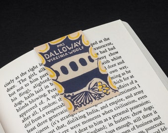 Puede incluir: Un marcapáginas con una ilustración azul y amarilla de un edificio con tres ventanas. El marcapáginas es para el libro "Mrs. Dalloway" de Virginia Woolf.