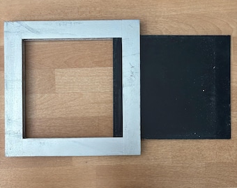 May include: A silver picture frame with a black backing. The frame is on a wooden surface.