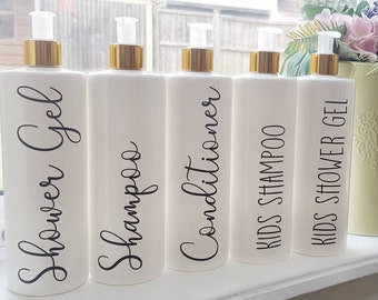 Könnte beinhalten: Fünf weiße Pumpflaschen mit schwarzen Etiketten. Die Etiketten lauten "Shower Gel", "Shampoo", "Conditioner", "Kids Shampoo" und "Kids Shower Gel".