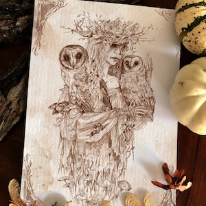Può includere: Illustrazione in seppia di una donna con una corona di rami, che tiene due gufi. L'opera d'arte ha un tema mistico e boschivo, con un lavoro di linea dettagliato e un'estetica vintage. Elementi decorativi: samare e zucche.