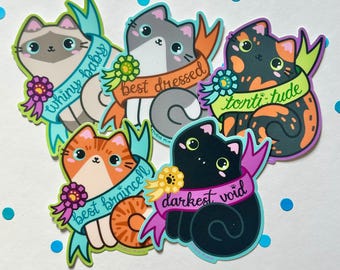 May include: Five colourful cat stickers with different personalities and slogans. The stickers feature a grey cat with "best dressed", a black cat with "darkest void", a calico cat with "torti-tude", an orange cat with "best braincell", and a grey and white cat with "whiny baby".