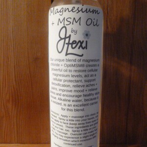 May include: A clear glass bottle with a white label that reads "Magnesium + MSM Oil by Fexi". The label describes the product as a unique blend of magnesium chloride and OptiMSM that creates a powerful oil to restore cellular magnesium levels, act as a cellular protectant, support detoxification, relieve aches and pains, improve mood and relieve stress, and encourage healthy skin tissue. The bottle is 9 oz.