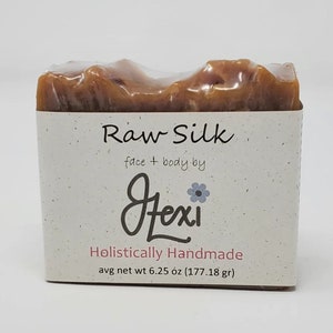 May include: A bar of Raw Silk face and body soap by Fexi, holistically handmade. The soap is a light brown color and has a translucent appearance. The soap weighs 6.25 ounces (177.18 grams).
