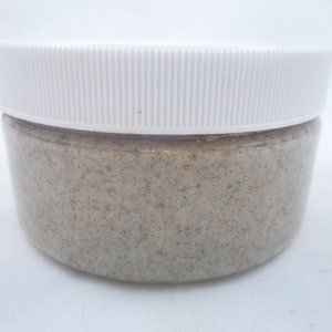 May include: A white plastic jar with a lid filled with a light brown scrub.