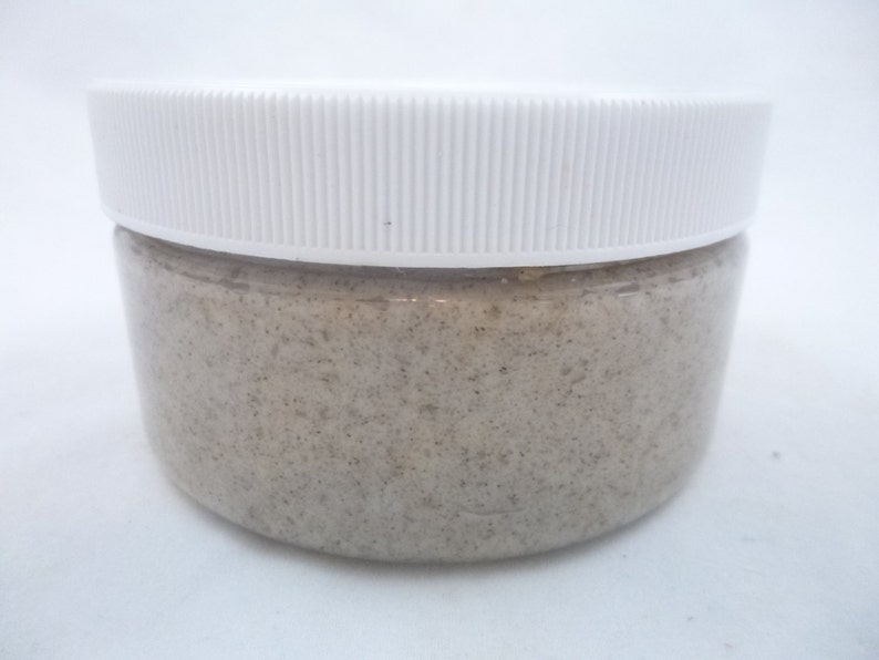 May include: A white plastic jar with a lid filled with a light brown scrub.