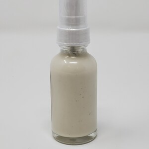 May include: A white plastic pump bottle with a clear glass container filled with a white cream-colored liquid.