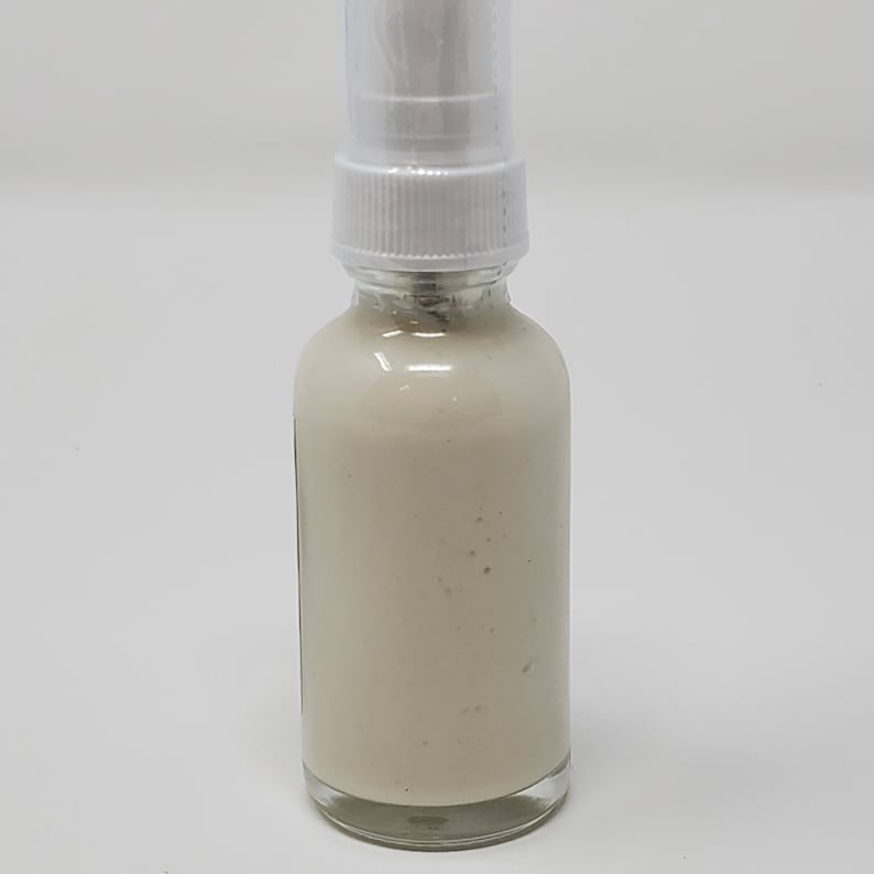 May include: A white plastic pump bottle with a clear glass container filled with a white cream-colored liquid.