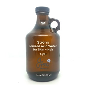 May include: A brown glass bottle with a handle, labelled "Strong Ionized Acid Water for Skin + Hair 4 pH" and "34 oz (963.88 gr)". The bottle has a white label with black text and a small flower graphic.