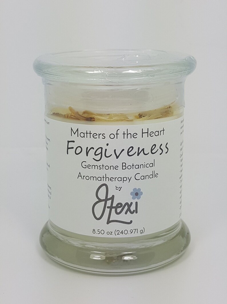 May include: A clear glass jar candle with a lid, labeled "Matters of the Heart Forgiveness." The candle is a gemstone botanical aromatherapy candle by Jlexi. It contains 8.50 oz (240.971 g) of wax and has a light-colored fill with visible botanicals.