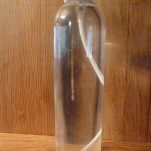 May include: A clear glass bottle with a white spray nozzle and a white plastic tube inside. The bottle is filled with a clear liquid.