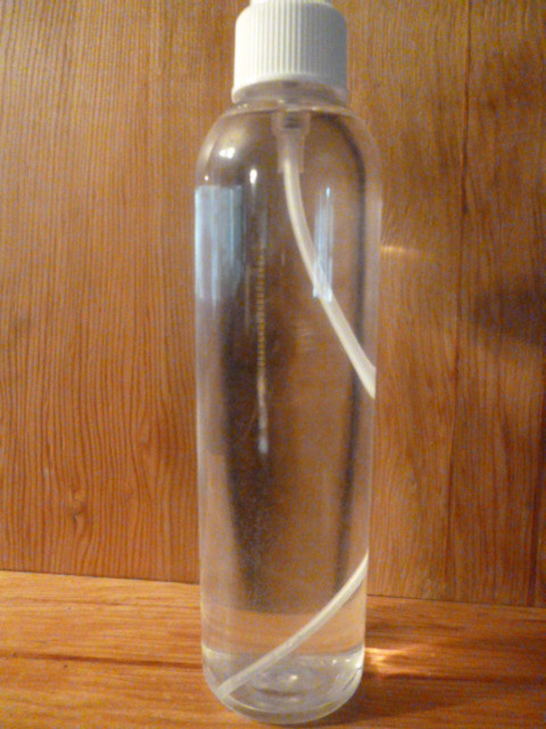 May include: A clear glass bottle with a white spray nozzle and a white plastic tube inside. The bottle is filled with a clear liquid.