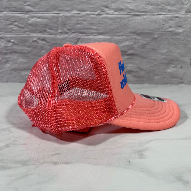 May include: A coral-colored trucker hat featuring a mesh back panel and a solid front panel with the blue text "float with" printed on the side. The cap includes a curved brim and a structured foam front, showcasing a vibrant monochromatic design.