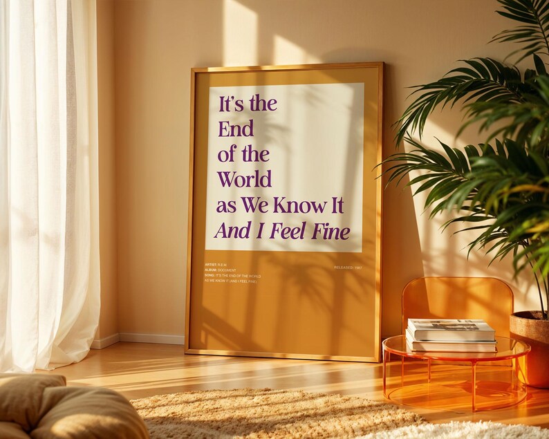 Puede incluir: Un p&oacute;ster enmarcado con el texto "It's the End of the World as We Know It And I Feel Fine" en morado sobre un fondo crema. El p&oacute;ster est&aacute; en una habitaci&oacute;n con una ventana, una planta y una peque&ntilde;a mesa naranja.
