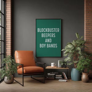 May include: A framed poster with the text "BLOCKBUSTER BEEPERS AND BOY BANDS" in white on a green background. An orange leather armchair with black metal frame sits in front of the poster. Potted plants and a small side table complete the room.