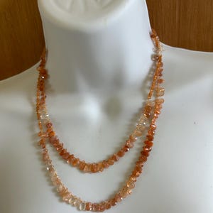 May include: A double-strand necklace made of orange and clear sunstone beads. The beads are faceted and have a natural, rustic look.