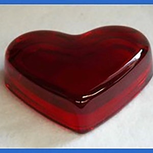 May include: A heart-shaped red glass trinket box. The box is made of clear glass with a deep red hue. It is a decorative item that can be used to store small items.