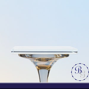 May include: A clear glass cake stand with a square top and a wide base. The stand is on a light blue background.