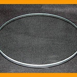 May include: A clear, circular glass object with a thin, reflective edge. The glass is set against a dark gray background, creating a contrast that highlights its shape. The object appears to be a decorative or functional item.