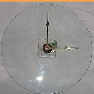 May include: A clear glass clock face with gold-colored hands. The clock face is blank, with no numbers or markings.