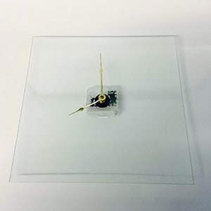 May include: A simple, modern clock with gold hands on a clear glass face.