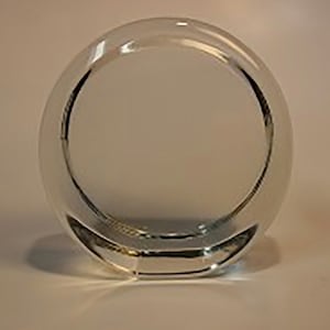 May include: A clear glass paperweight in the shape of a circle.