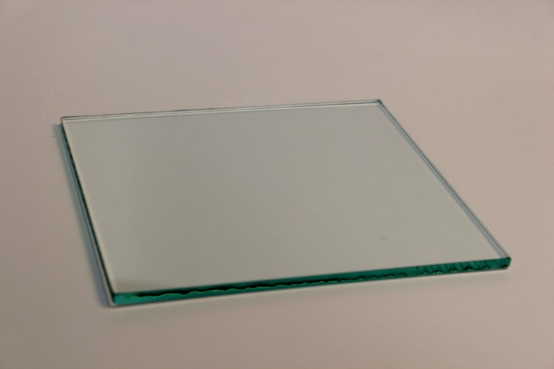 May include: A clear, square glass pane, likely for a picture frame or similar use. The glass is transparent, with a slight green tint visible at the edges. The pane is approximately 10 inches by 10 inches.