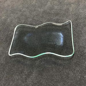 May include: A clear glass tray with a wavy edge. The tray is on a dark gray surface.