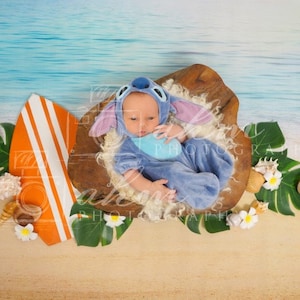 Puede incluir: Un beb&eacute; con un disfraz azul de Stitch est&aacute; acostado en un cuenco de madera con una tabla de surf y hojas tropicales sobre un fondo de playa.