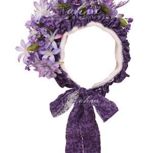 May include: Purple flower crown headband with a white fabric base and a purple satin bow. The headband is decorated with purple flowers and leaves.