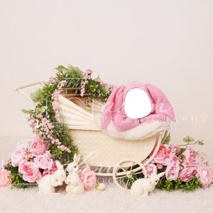 May include: A white baby carriage with pink fabric and a white blanket inside. The carriage is surrounded by pink flowers and green leaves. There are also three white bunny figurines in front of the carriage.