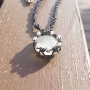 May include: A black cord necklace with a white glass pendant surrounded by silver beads.