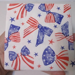 Pode incluir: Um guardanapo de papel quadrado com um padrão repetitivo de laços e estrelas. Os laços são decorados com listras vermelhas e brancas e seções azuis com estrelas brancas. Pequenas estrelas vermelhas e azuis estão espalhadas pelo fundo branco.