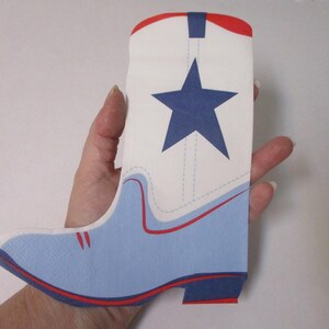 Pode incluir: Um recorte de papel plano em forma de bota, apresentando uma seção superior branca com uma grande estrela azul-marinho, uma área de pé azul-claro e linhas vermelhas de destaque ao longo da ponta, do calcanhar e da borda superior.