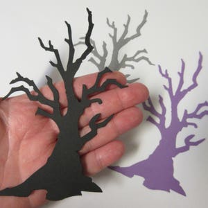 Pode incluir: Tr&ecirc;s recortes de papel de &aacute;rvores nuas em preto, cinza e roxo. As &aacute;rvores est&atilde;o em uma m&atilde;o, com a &aacute;rvore preta em primeiro plano.