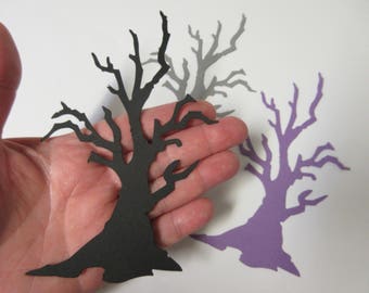 May include: Three paper cutouts of bare trees in black, gray, and purple. The trees are in a hand, with the black tree in the foreground.