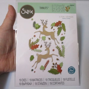 May include: A package of 19 die-cut metal craft dies featuring a design of two deer with antlers, leaves, and acorns. The dies are from the Sizzix brand and are designed by Lisa Jones. The package is labeled "Thinlits" and has the product number 665945.