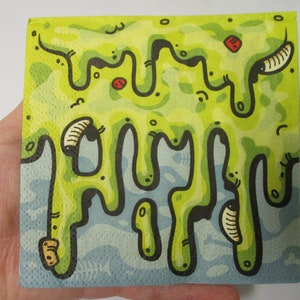 May include: A square, hand-drawn illustration on a napkin featuring a green, drippy design with black outlines and small red accents. The bottom portion has a blue water-like pattern with fish bones.