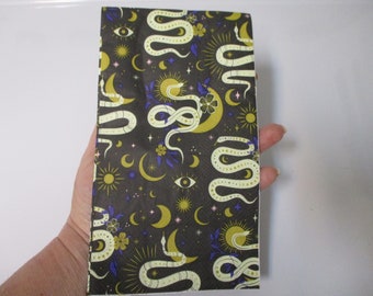 May include: A black fabric with a repeating pattern of white snakes, gold moons, and stars. The snakes are intertwined with each other and with the moons and stars. The fabric has a dark background with a subtle texture.
