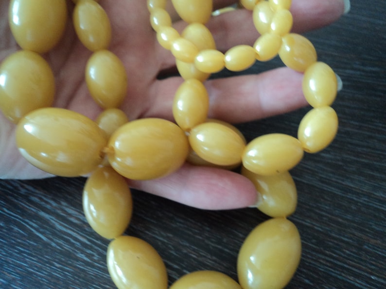 Pode incluir: Um longo fio de contas de &acirc;mbar amarelo de forma oval. As contas s&atilde;o enfiadas em um cord&atilde;o e est&atilde;o dispostas em um padr&atilde;o solto e fluido.