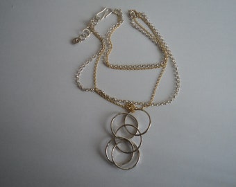 May include: A silver and gold chain necklace with a pendant made of four interlocking circles.