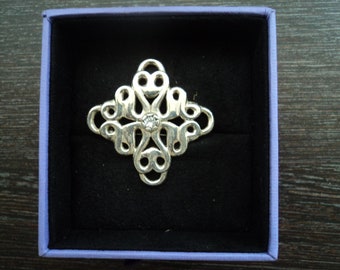 May include: A silver brooch with a decorative design featuring a central clear rhinestone. The brooch is displayed in a purple velvet box.