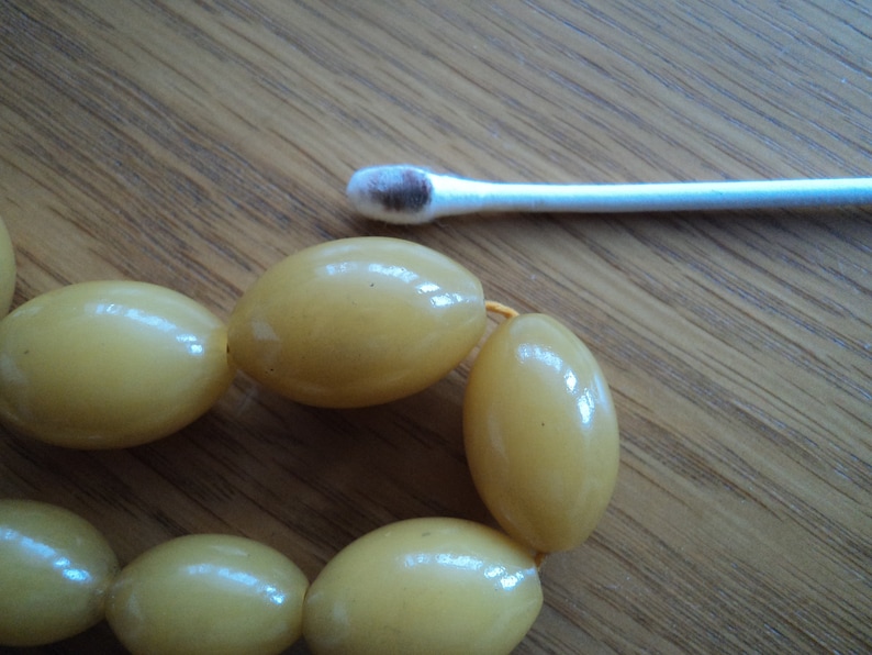 Pode incluir: Um close-up de uma corda de contas ovais amarelas. As contas s&atilde;o enfiadas com um fio fino amarelo. As contas s&atilde;o lisas e brilhantes.