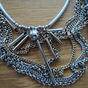 Peut inclure: Un collier multi-rangs argent et or avec un grand pendentif argent et de multiples maillons de chaîne.