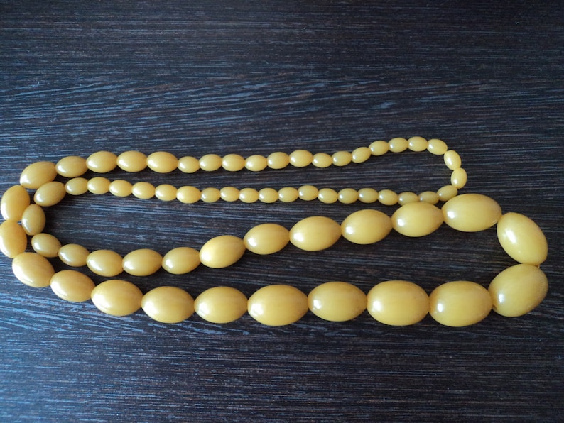 Pode incluir: Um colar longo de contas de pl&aacute;stico amarelo com contas ovais grandes. O colar &eacute; composto por duas fileiras de contas menores.