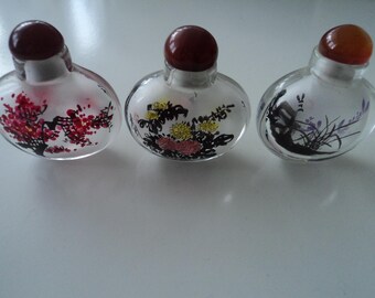 May include: Three small, round, clear glass bottles with red, orange, and brown stoppers. Each bottle has a different black and white ink painting on the front. The paintings depict flowers, a tree, and a bird.
