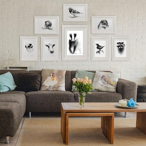 K&ouml;nnte beinhalten: Eine Wand mit gerahmten Schwarz-Wei&szlig;-Tierdrucken, darunter ein Dachs, V&ouml;gel und eine Kuh, an einer wei&szlig;en Backsteinmauer. Ein braunes Ecksofa mit dekorativen Kissen und ein Holztisch vervollst&auml;ndigen die Wohnzimmereinrichtung.
